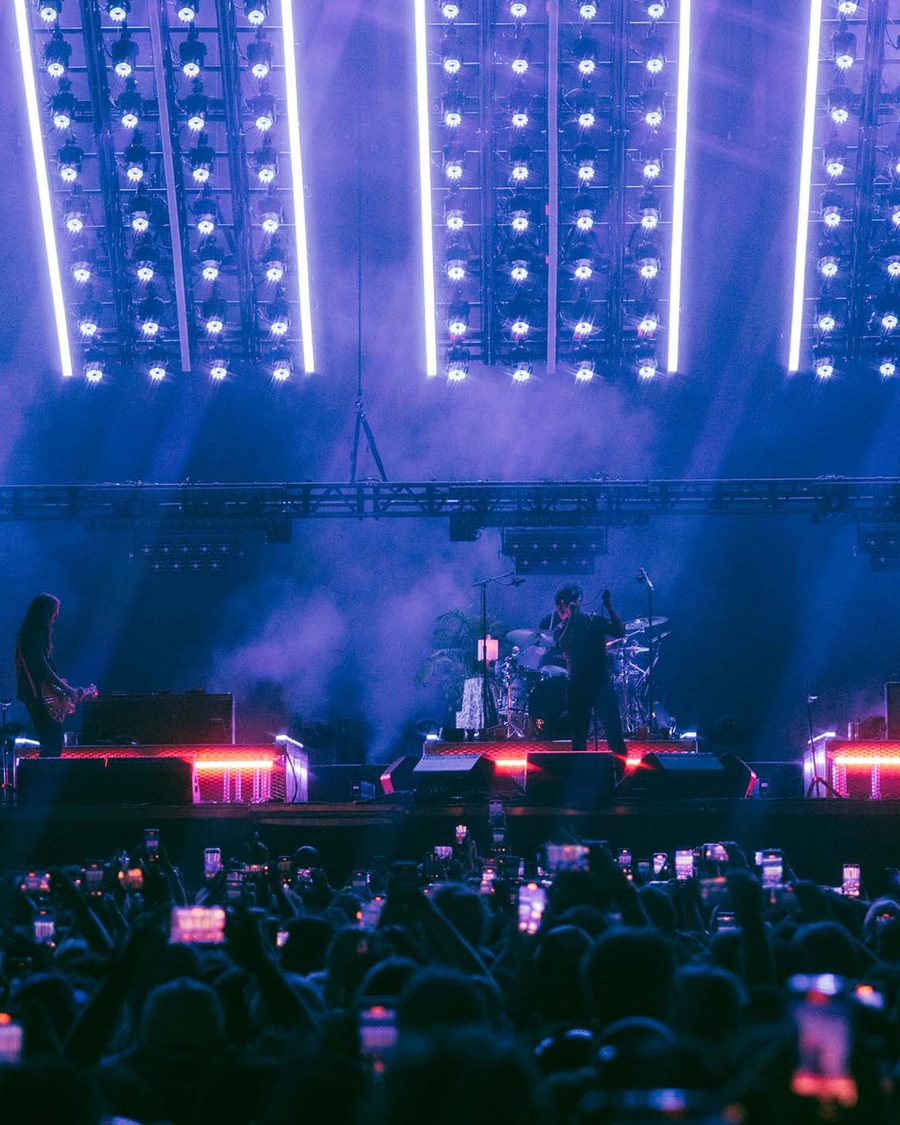 The Strokes on an outdoor stage under a grid of white lights with a crowd in front - the official tour image