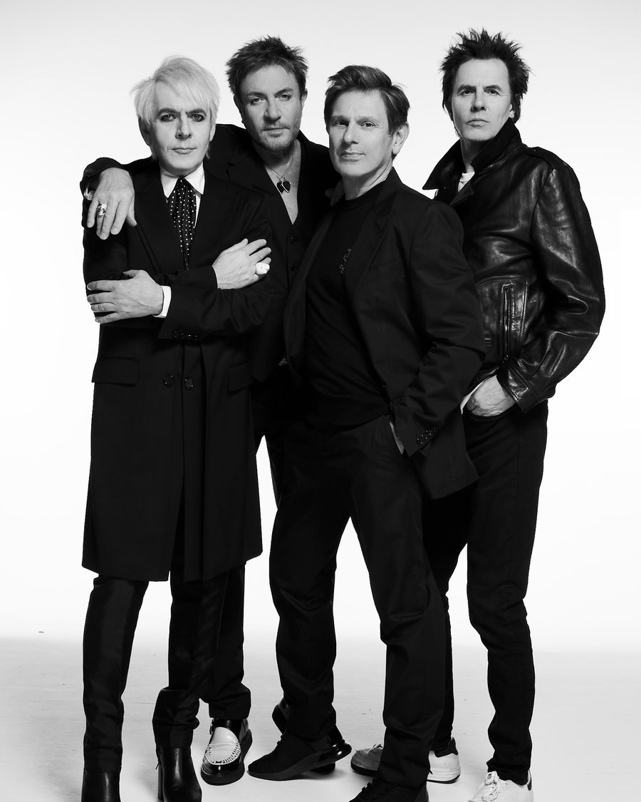 Duran Duran, the four members in black coats in a black-and-white studio portrait - the official tour image