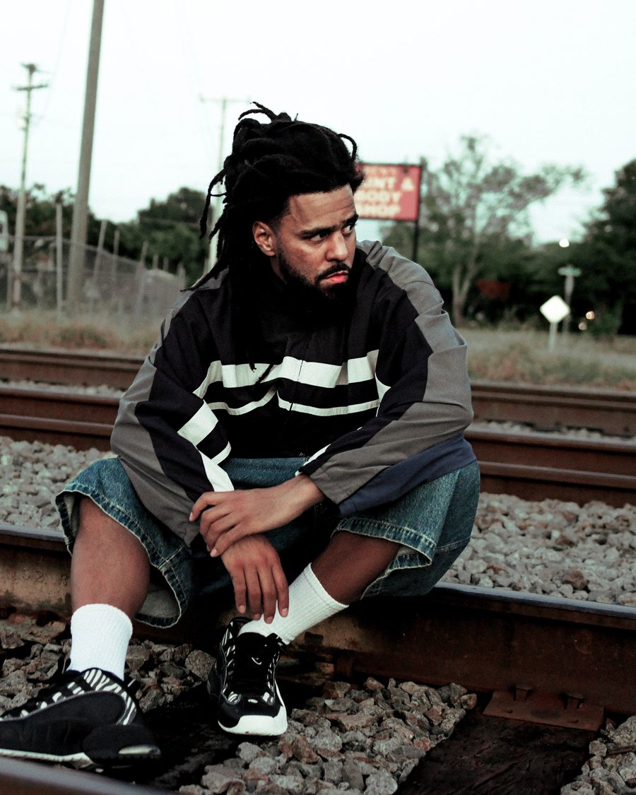 J. Cole crouched on railway tracks in a striped jacket - the official Fall-Off Tour image