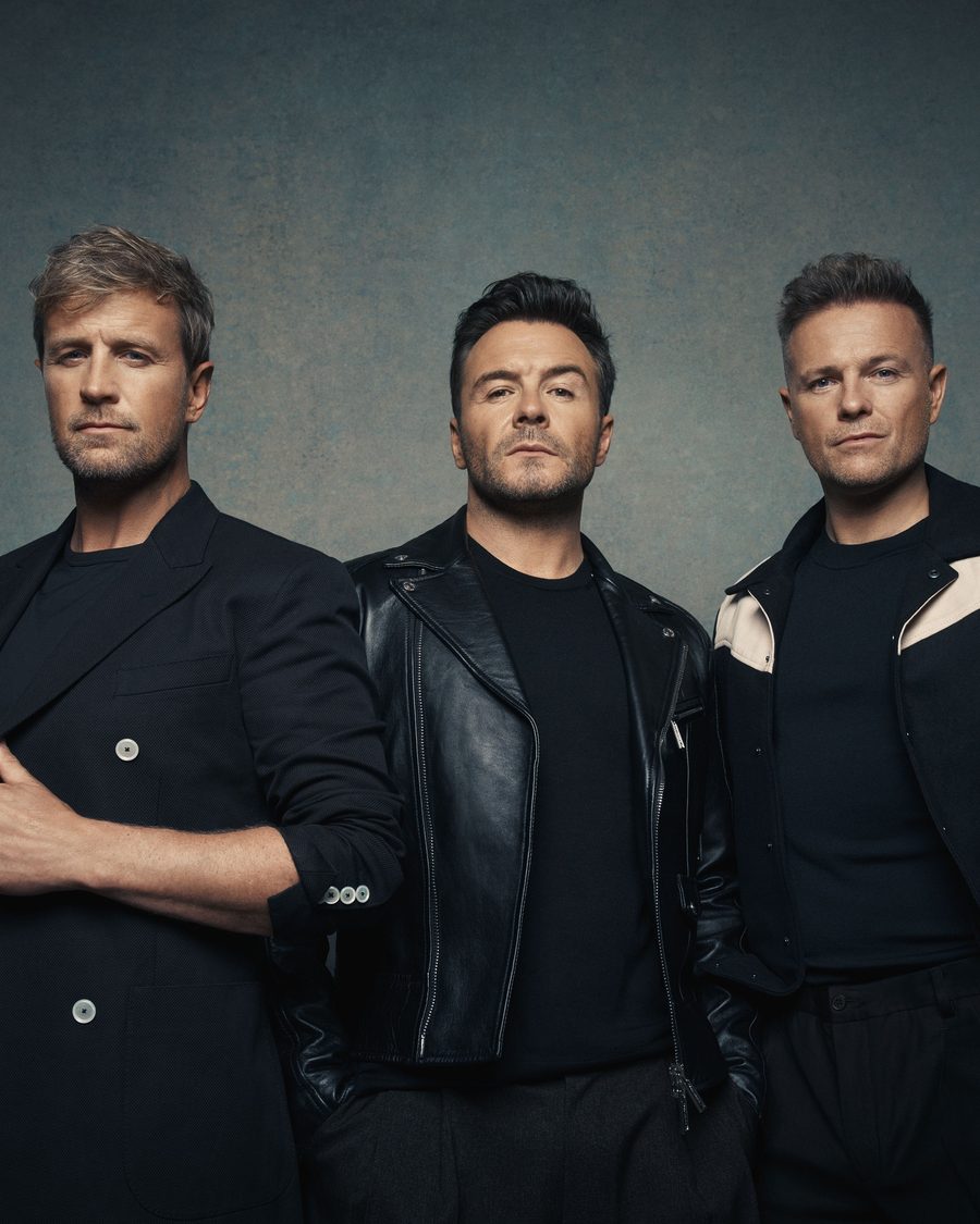 Westlife - Kian Egan, Shane Filan and Nicky Byrne in black jackets against a grey studio backdrop - the official Westlife 25 tour image